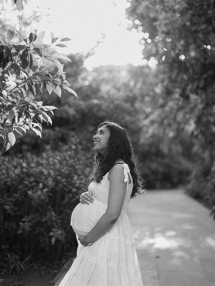 A gorgeous black and white portrait of a mother-to-be in a garden. She looks up towards the light with a hopeful and happy expression, full of anticipation.