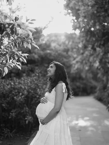 A gorgeous black and white portrait of a mother-to-be in a garden. She looks up towards the light with a hopeful and happy expression, full of anticipation.