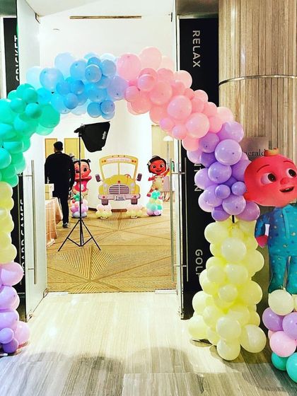 A cheerful rainbow balloon arch welcomes guests to a Cocomelon party, with a life-sized JJ character cutout greeting everyone at the entrance.