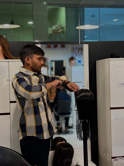 A student practices a layered haircut on a mannequin, carefully checking his sections and guidelines. This repetitive practice is key to developing muscle memory and consistency.