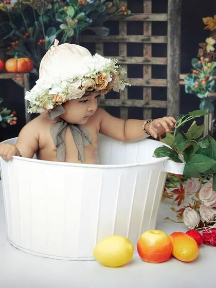 A baby in a floral bonnet curiously explores the props during a bathtub photoshoot. We create a safe and fun environment for these splashy sessions.