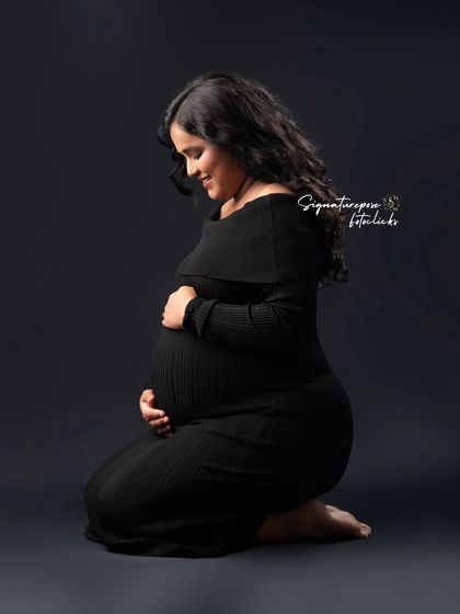A kneeling portrait in a simple black dress, creating a timeless and elegant silhouette against the dark backdrop.