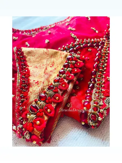 A close-up of a heavily embellished blouse sleeve, featuring 3D floral details, beads, and zardosi work on a vibrant red fabric.