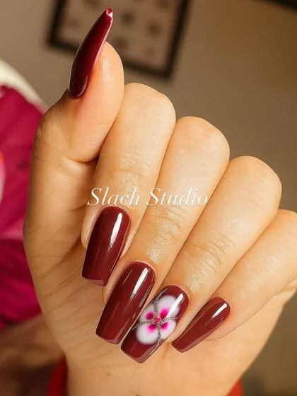 A closer look at the hand-painted flower on these long, coffin-shaped nail extensions. The blend of white and pink creates a realistic, layered effect against the bold maroon base.
