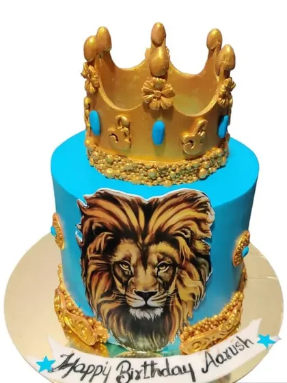 A majestic lion-themed cake for a little king. The cake is a vibrant blue, decorated with a realistic lion portrait and a golden crown on top.