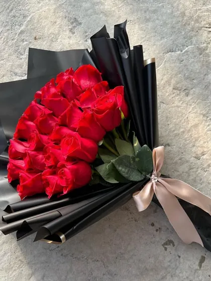 A timeless classic with a modern twist. This chic hand bouquet features a dense gathering of vibrant red roses, elegantly wrapped in sophisticated black paper and tied with a champagne-colored ribbon.