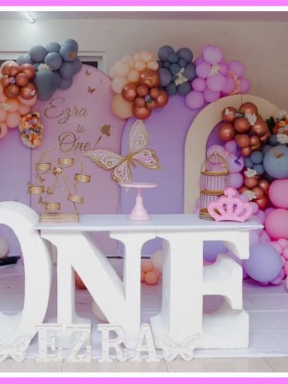 A sophisticated butterfly-themed first birthday. The decor uses a muted color palette of peach, grey, and pink, with a large 'ONE' table and elegant butterfly accents.