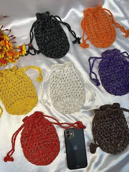 This image displays a variety of my handmade crochet potli bags in seven different shimmering colors, including black, orange, and purple. An iPhone is shown for size reference.