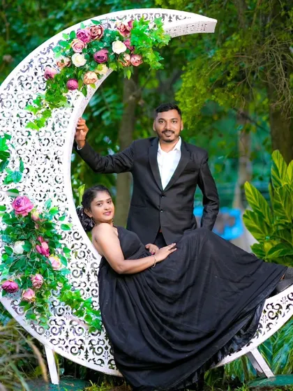 A whimsical shot with the couple posing on a large, crescent moon prop decorated with flowers. Their black outfits contrast beautifully with the white moon.