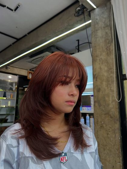 This is the trendy 'hush haircut' paired with a warm auburn color and bangs. The soft layers and face-framing pieces create a romantic and wearable style.