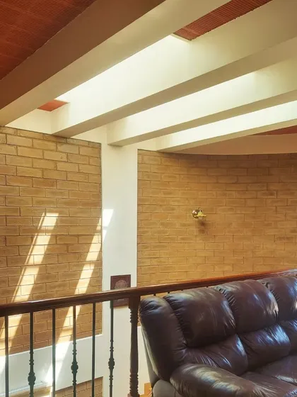 Sunlight streams from a skylight, creating bold diagonal stripes across exposed brick walls, demonstrating the dynamic and ever-changing quality of natural light.