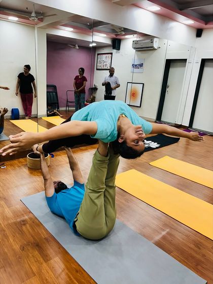 A student balances gracefully in a flying plank pose during an Acro Yoga session. The joy and confidence on her face is what this practice is all about.