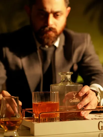 A sophisticated lifestyle shot featuring a man in a suit with a decanter of Glenfiddich whisky. The moody lighting and formal attire create an aspirational and premium brand image.