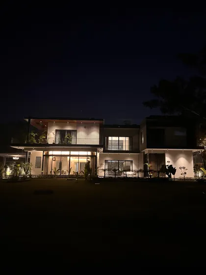 A wide shot of 'The One' at night. The facade lighting reveals the layered levels of the elevation and the careful composition of stone, wood, and glass.