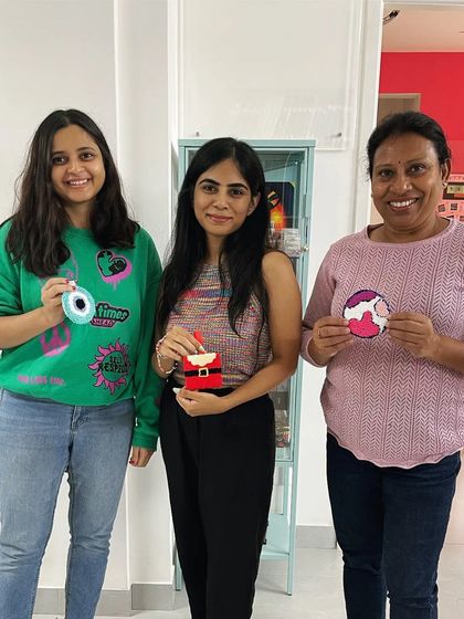 Three participants showing their unique creations: an evil eye charm, a Santa ornament, and a planet Earth design. The variety is always inspiring.