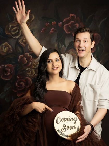 A joyful and energetic pregnancy announcement. The couple holds a "Coming Soon" sign, and the partner waves excitedly at the camera.