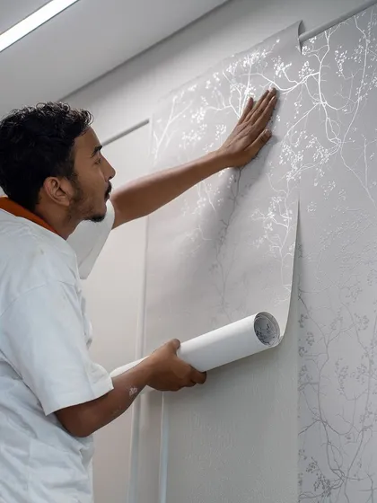 Our trusted wall-covering partner at work. A skilled installer carefully applies a delicate silver botanical wallpaper, showcasing the precision and care that goes into every project we undertake.