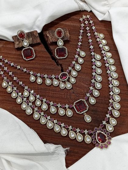 A grand, three-layered AD necklace set. This piece is designed for maximum impact, featuring square and teardrop stones, and is available in blue, green, pink, and red.