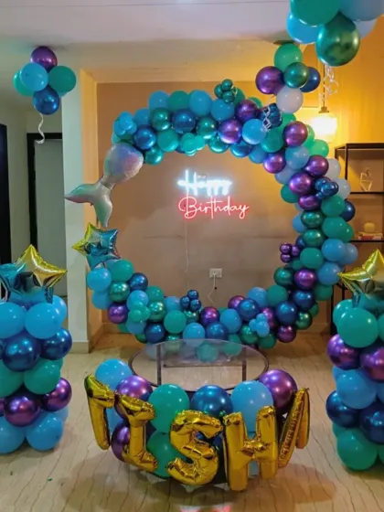 A mermaid-themed balloon ring in shades of blue, purple, and teal, with foil name balloons.