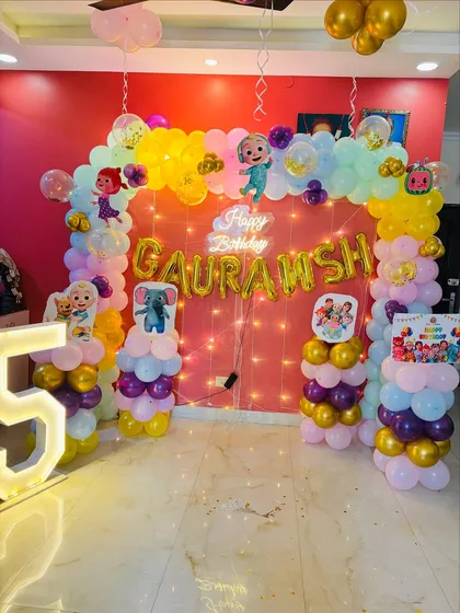 A grand Cocomelon themed decoration for a 5th birthday. This setup includes a large balloon arch, character cutouts, and a light-up marquee number '5'.