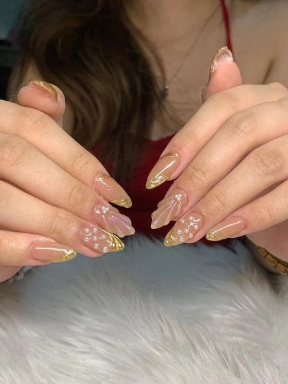 A glamorous set of stiletto extensions with a nude base, gold chrome tips, and delicate 3D shell and pearl accents.