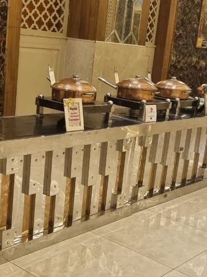 A sleek, modern buffet counter with a silver and gold metallic finish. This setup includes traditional copper serving pots, blending contemporary design with classic Indian serveware.