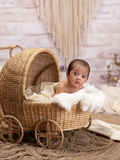 A curious newborn peeks out from a vintage-style rattan pram. The bohemian-inspired set with macrame and pampas grass creates a trendy and stylish look.