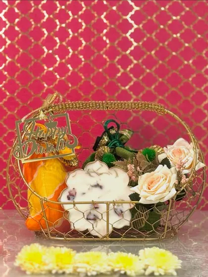 A golden wire basket filled with our signature 'Blooming Essence' Diya, potlis, and artificial flowers. This hamper is designed to fill any home with warmth and festive charm.