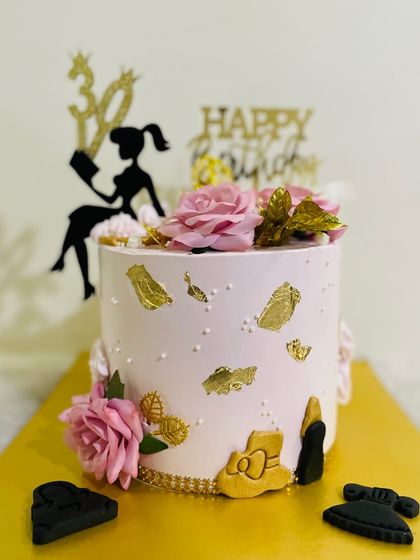 A chic cake for a "boss lady," decorated in soft pink with gold leaf, high heels, and a silhouette of a woman reading.