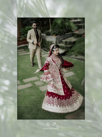 A dynamic shot of the bride twirling in her elaborate red lehenga, with the groom walking behind her.