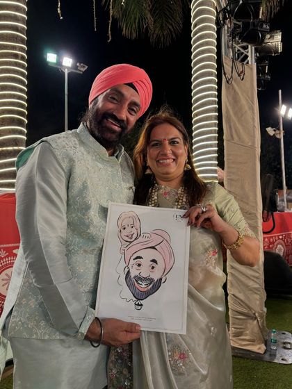 A couple holding their caricature at an outdoor wedding. The festive lights in the background create a beautiful ambiance.