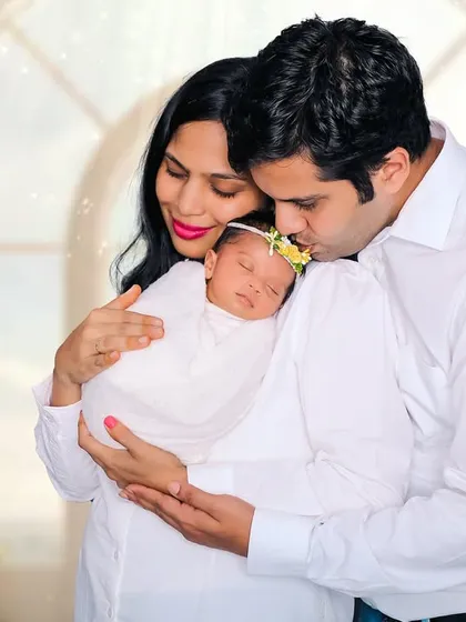 A tender moment as parents welcome their new baby. The father kisses the baby's head while the mother holds her close, creating a portrait filled with love.