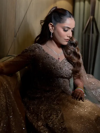 The bride looks radiant and happy, with her wavy ponytail adding a touch of playful elegance to her sparkling Sangeet gown.