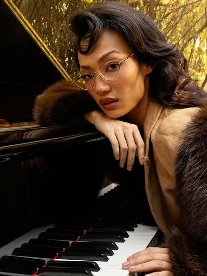 A classic, elegant portrait of the female model from the John Jacobs "Winter Edit" shoot, leaning on the piano.