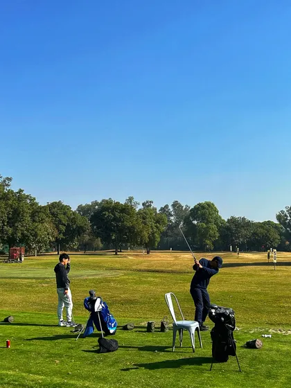 Two golfers practice their swings on a bright and sunny day, with their bags resting beside them.
