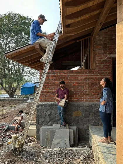 There is no substitute for being on-site to resolve complex details. Here, our principal architect is up on a ladder, working directly with the team to finalize the roofing details for the farmhouse.