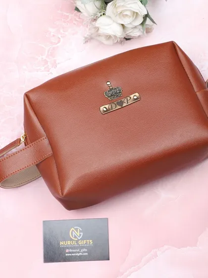 The personalized leather pouch in a rich tan color, customized with a name and crown charm.