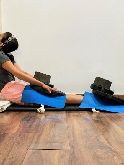 Weights are used here in a supported Dandasana (Staff Pose) to quiet the nervous system. The gentle pressure on the thighs helps to ground the body, release tension in the leg muscles, and pacify a restless mind.