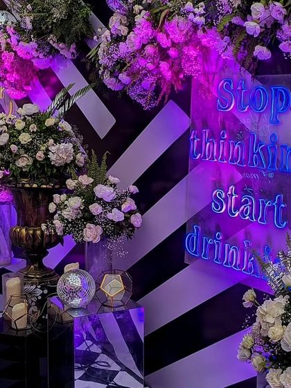 A close-up of the fun and quirky details at a Sangeet. A neon sign with a playful message, 'Stop thinking start drinking,' adds a lighthearted and modern touch to the bar area.