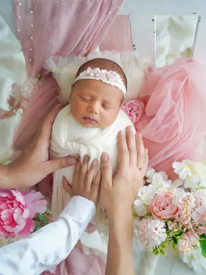 The parents' hands gently cradle their baby, adding a personal and loving touch to this beautifully styled floral portrait.