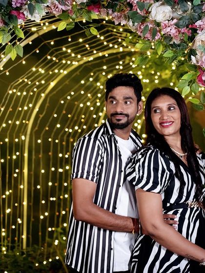 A beautiful portrait of a couple in matching striped outfits, framed by a floral and light arch.