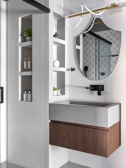 This bathroom combines a concrete-finish sink with a warm wood vanity. The unique shield-shaped mirror and modern light fixture add an artistic touch, while the built-in shelving provides practical storage.