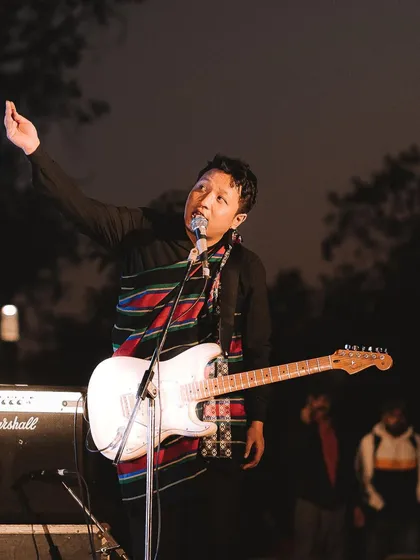 A musician on stage, raising a hand to connect with the audience while playing his guitar. It's these small, authentic interactions that I love to photograph.