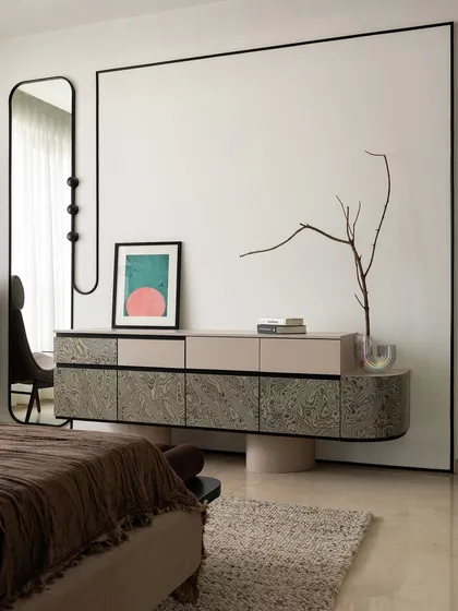 The floating console and full-height mirror create a sense of lightness in the bedroom. The blank wall space is intentional, allowing the custom furniture and curated art to become the focus, embodying our 'less is more' approach.