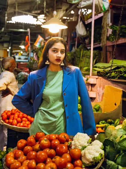 High fashion meets a local vegetable market. The contrast between the model's sharp blue blazer and the earthy colors of the produce creates a striking image.
