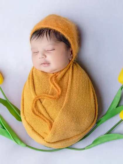 A simple, elegant shot of a newborn wrapped in a mustard-colored swaddle, framed by yellow tulips.