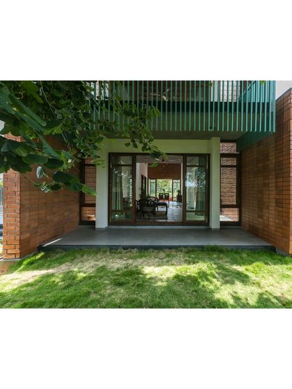 The exterior of 'An Earthy Affair' shows how the home opens up to the garden. The use of exposed brick and a green-painted balcony railing connects the structure to its natural surroundings.