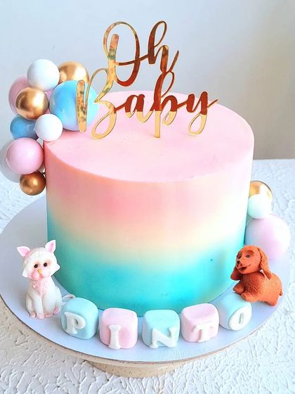 A baby shower cake with a pink and blue ombre effect, decorated with balloon spheres and cute animal toppers.