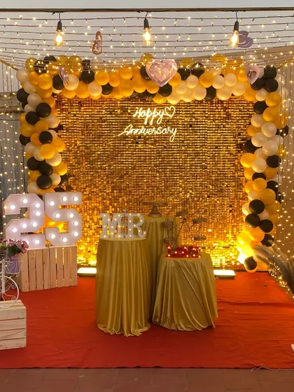 Here is a 25th-anniversary party I decorated on a terrace. The setup includes a brilliant gold shimmer wall, a full balloon arch, and large marquee numbers, all under a canopy of warm fairy lights.