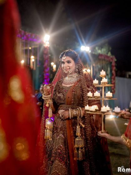 A beautiful shot of the bride making her entrance, escorted by women holding traditional candle stands, creating a serene and divine atmosphere.